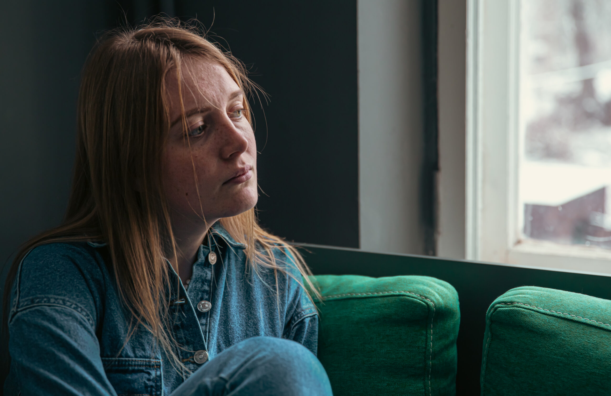 A beautiful young woman is sitting on the sofa by the window on a cold winter day.